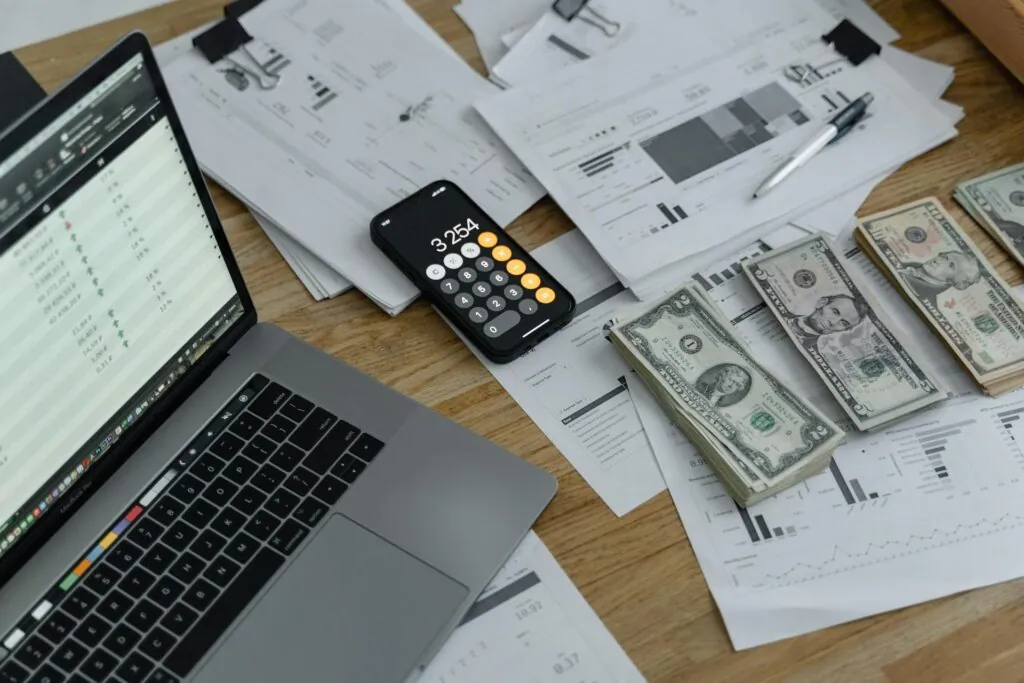 Dollars in cash on desk next to calculator and laptop